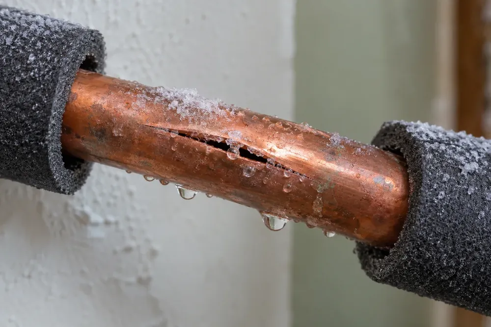Split copper pipe with frost crystals and droplets along the crack, insulation pulled back