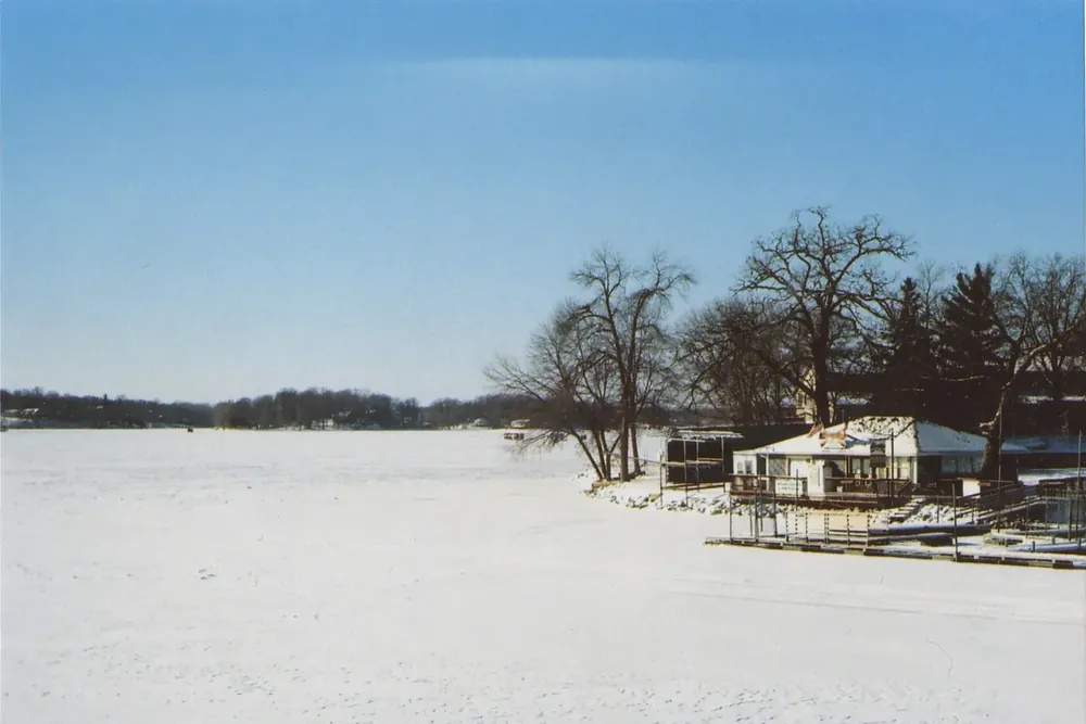 Frozen Prior Lake with a lakeside boathouse and bare trees in winter, Minnesota